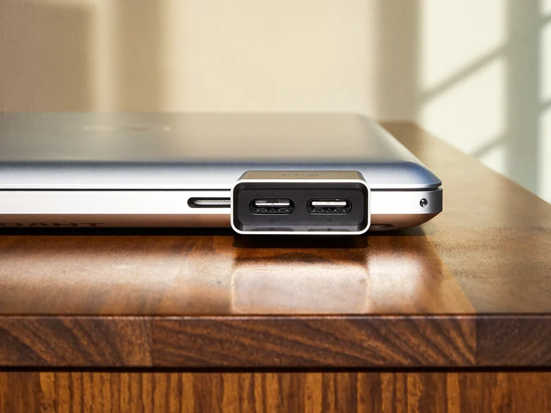 Kompakter Aluminium-Hub seitlich an einem flachen Laptop auf einem Holzschreibtisch
